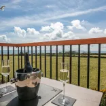 A wine bucket and glasses on a balcony table with views in the sunshine.