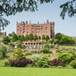 Gardens in front with Powis Castle on the horizon against blue sky.